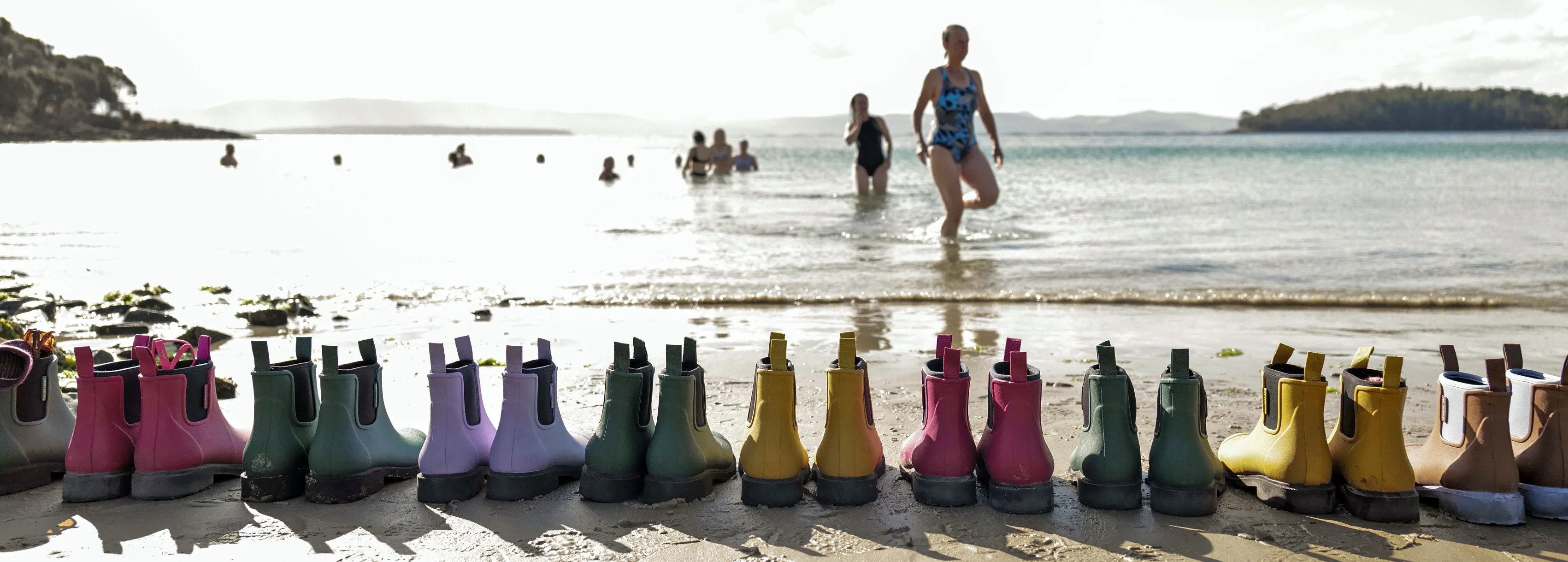 A line of Merry People boots are set against the shore line of a beach